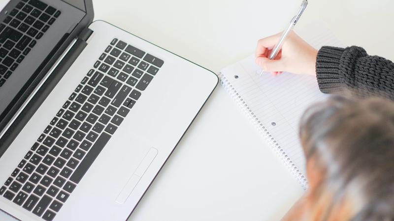 Person watching laptop whilst taking notes in notebook