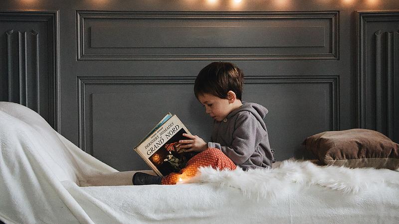 Small child reading in bed with fairy lights