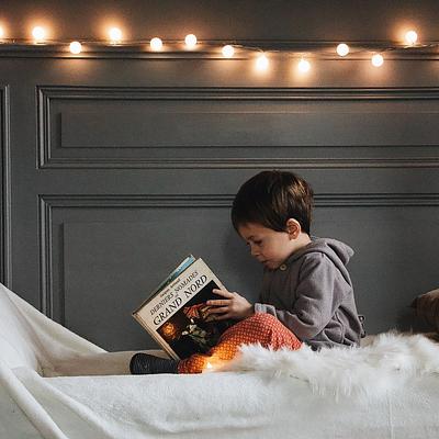 Small child reading in bed with fairy lights