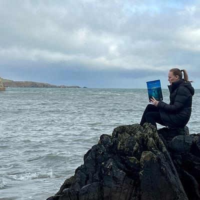Woman sitting on sea rocks with book