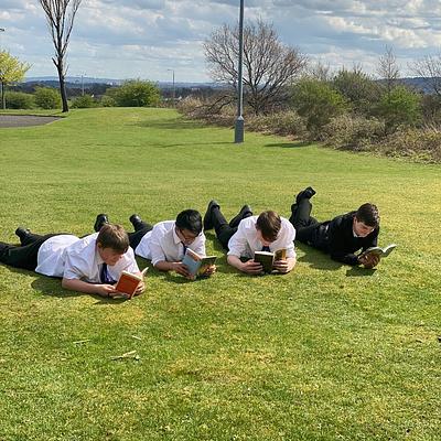 A row of four pupils lying on their stomachs reading on the grass