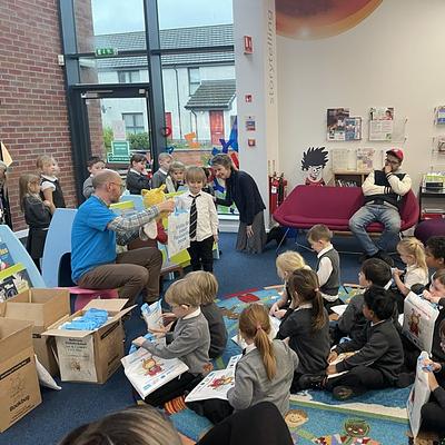 Primary 1 pupils sitting on a library floor, holding bookbug bags